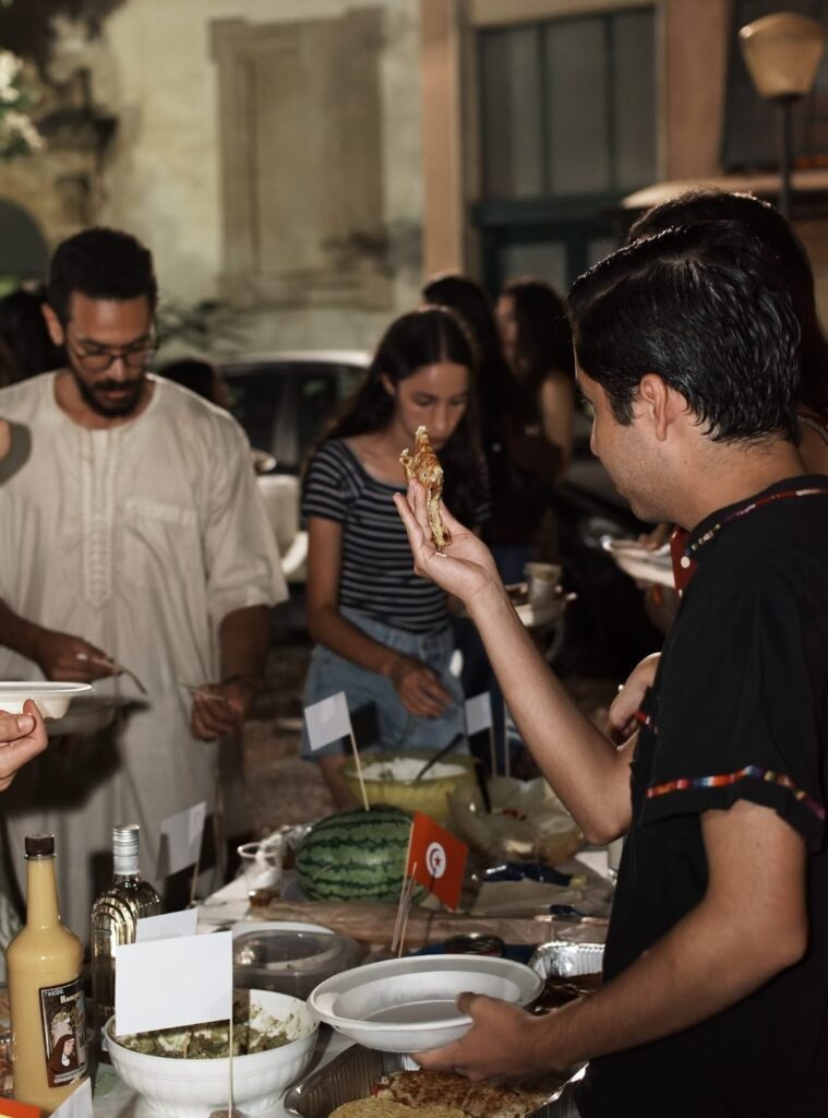Students sharing dishes from their home countries at an evening international food night, with small national flags on the table